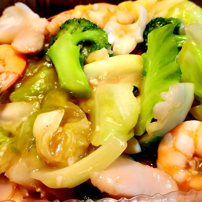 Close-up of Red Bowl Noodles' Chinese dish with shrimp, broccoli, and cabbage in a savory sauce.
