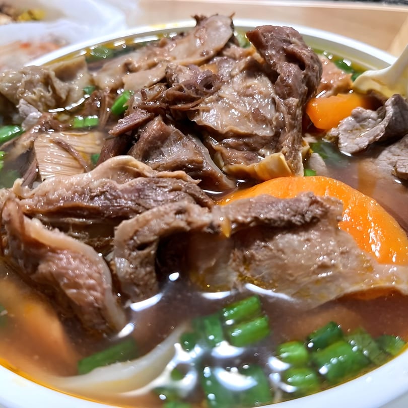 Close-up of Red Bowl Noodles' beef noodle soup with carrots and green onions.
