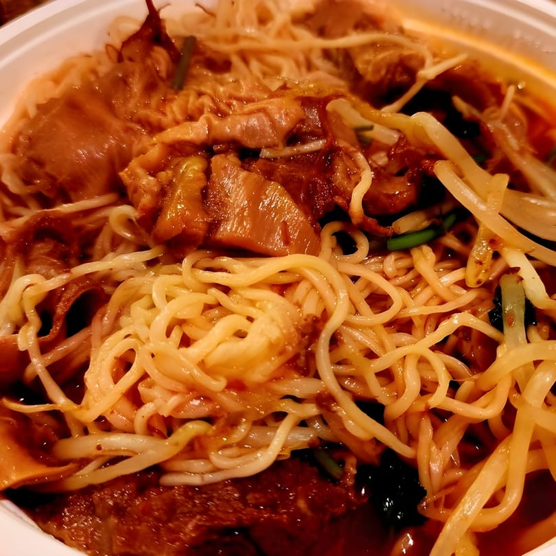 Close-up of Red Bowl Noodles' Chinese dish with noodles, meat, and vegetables in a rich sauce.